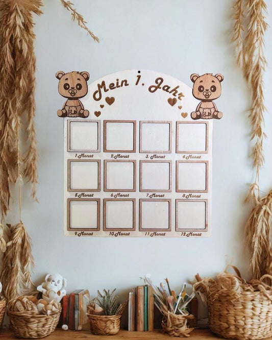 Holz-Meilensteintafel für Babys mit dem Text "Mein 1. Jahr" und 12 Fotoschlitzen. Oben befinden sich zwei Teddybär-Ausschnitte. Die Tafel ist aus hellbraunem Holz gefertigt und dient zur Anzeige der monatlichen Fotos des Babys.