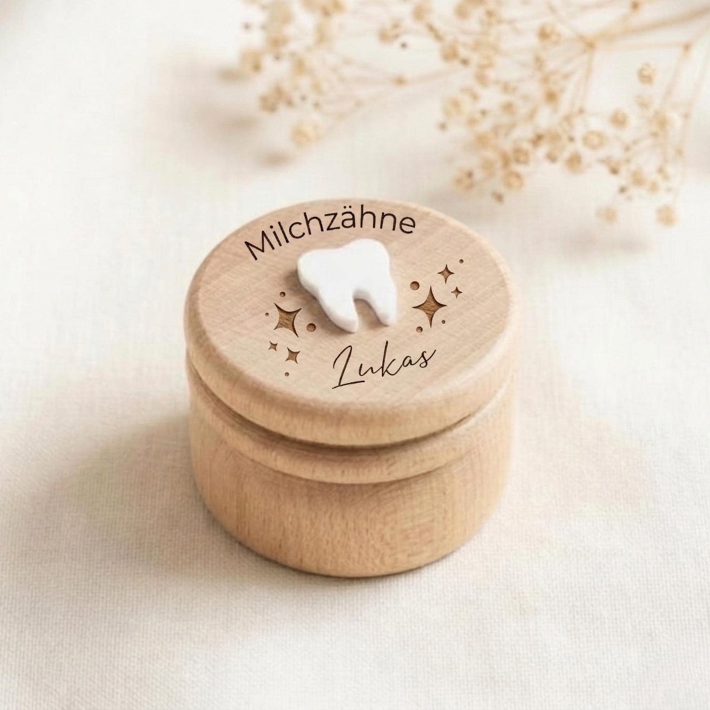 Könnte beinhalten: Kleine, runde Holzkiste mit Deckel. Der Deckel trägt die Aufschrift "Milchzähne" und "Lukas", ein weißes Zahn-Ornament und Sternenmuster. Die Kiste ist hellbraun und hat eine natürliche Holzmaserung.